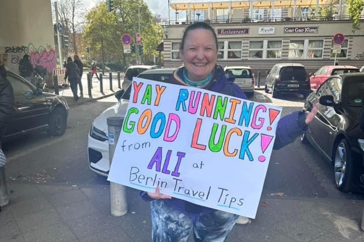 Ali cheering at the Berlin Marathon, holding a sign that says "Yay running! Good luck! from Ali at Berlin Travel Tips"